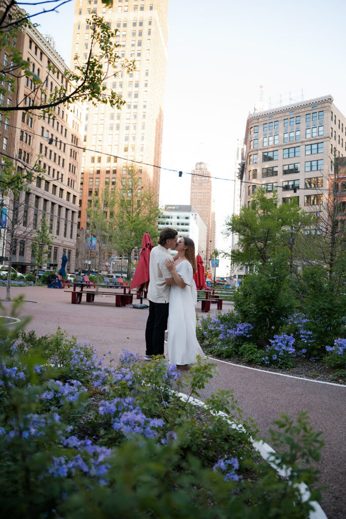 Couple kissing in a flower garden with downtown Detroit buildings in the background.