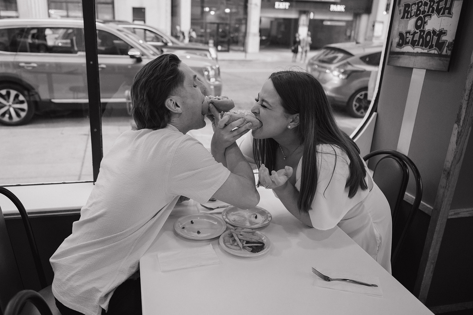 Couple taking a bite of coney dogs together at American Coney Island during their engagement session.