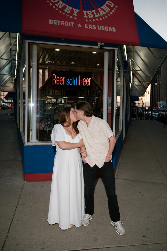 Couple kissing outside American Coney Island at dusk during their Detroit engagement photos.