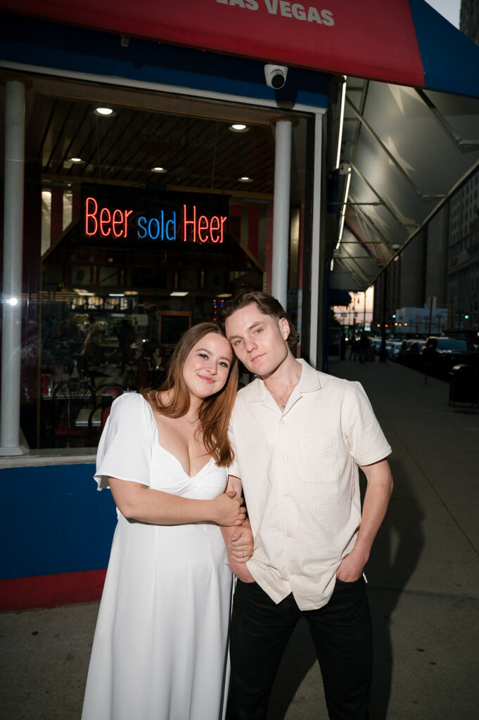 Couple posing outside American Coney Island at dusk during their Detroit engagement photos.