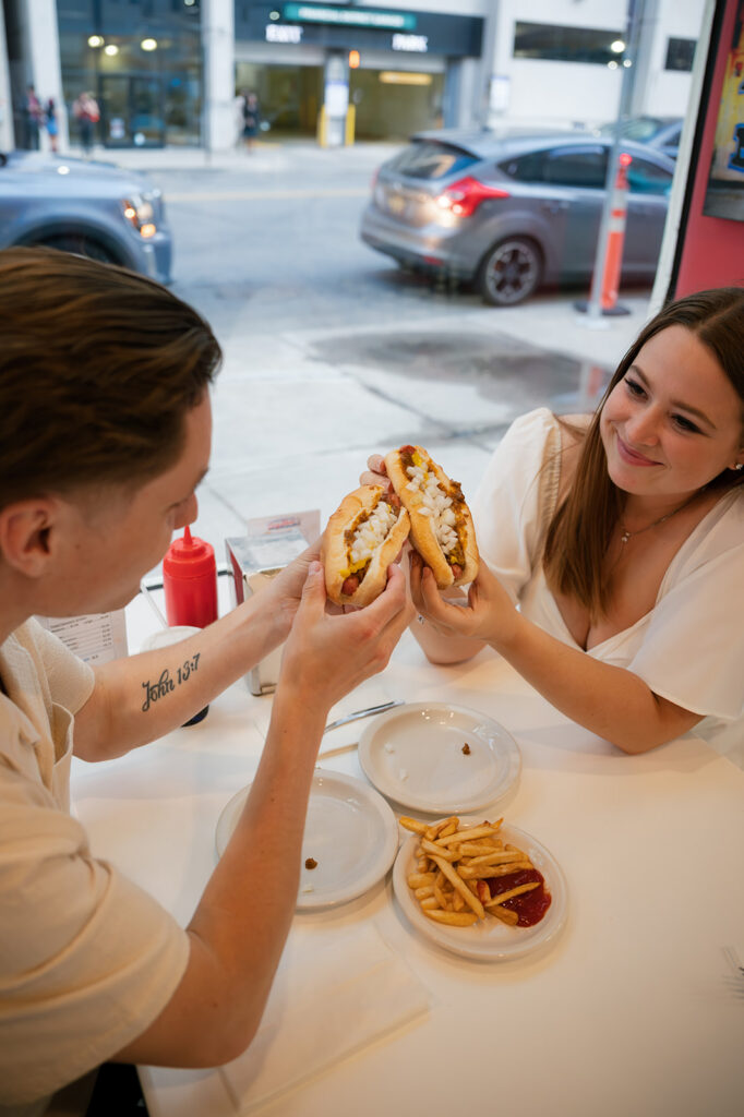 Couple toasting coney dogs inside American Coney Island during their downtown Detroit engagement photos.