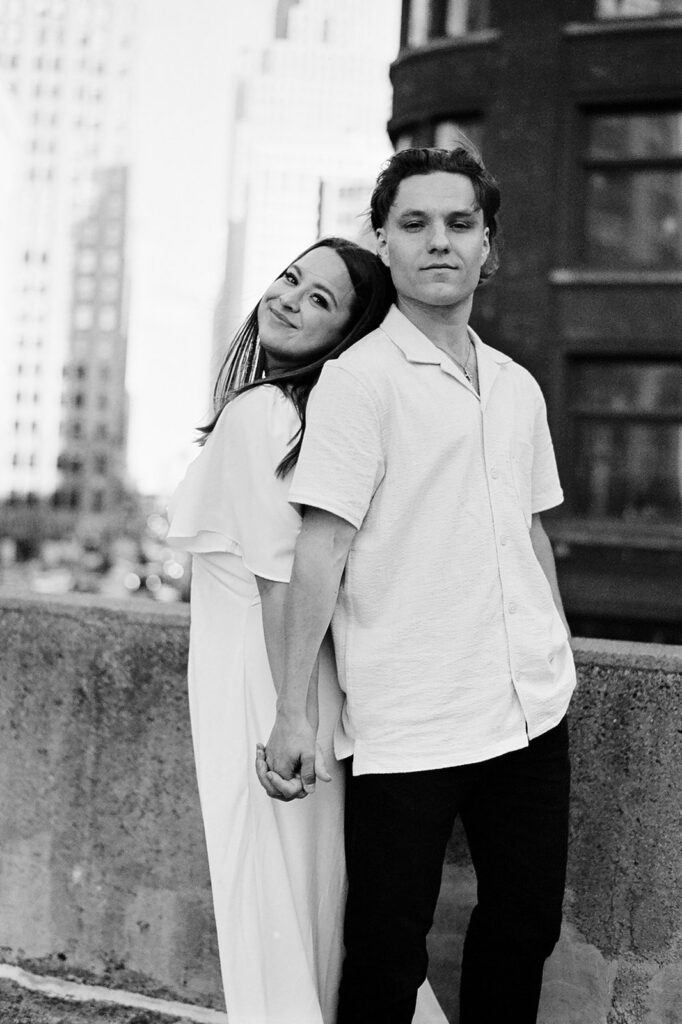 Black and white 35mm film photo of a couple standing with their backs together while holding hands.