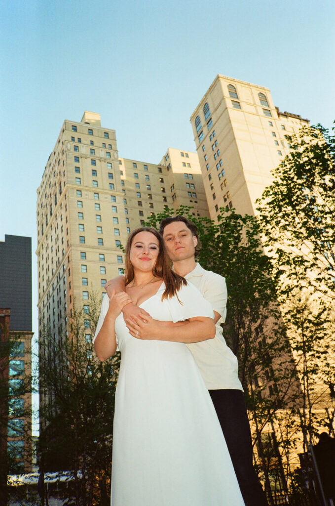 35mm film photo of a couple from below with the city skyline behind them.