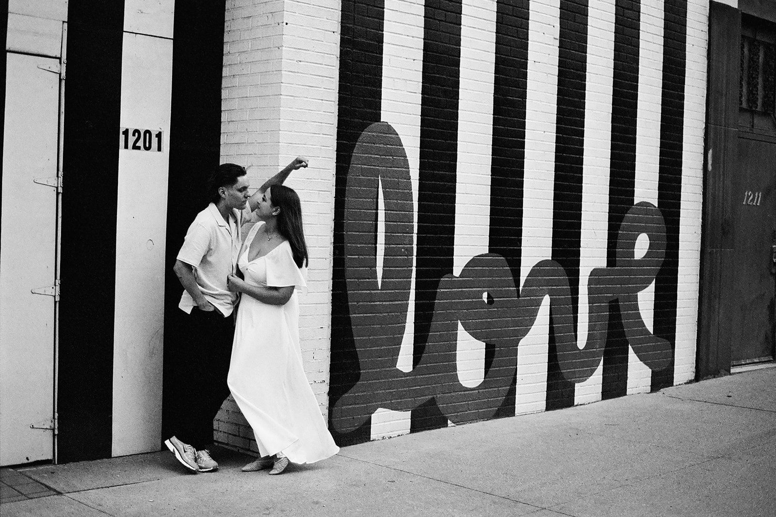 Black and white 35mm film photo of a couple posing next to a downtown Detroit mural that says love.