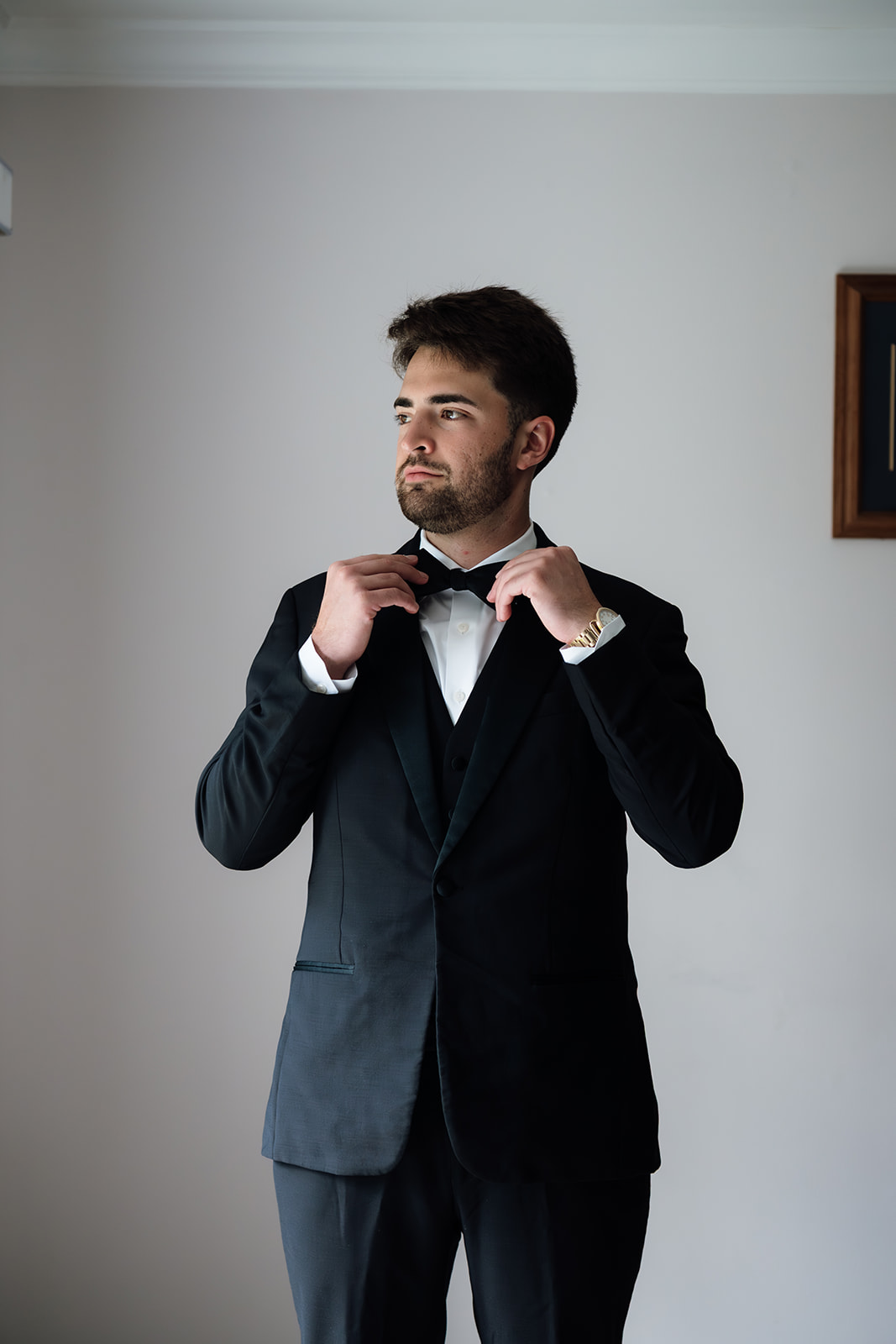 Groom adjusting his bow tie while getting ready in a black tux before the wedding ceremony.