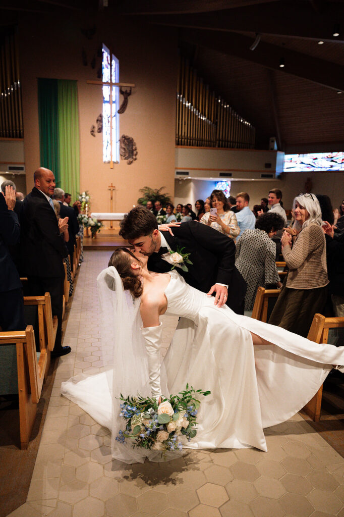 Bride and grooms end of aisle dip kiss at St. Edith Catholic Church in Livonia.