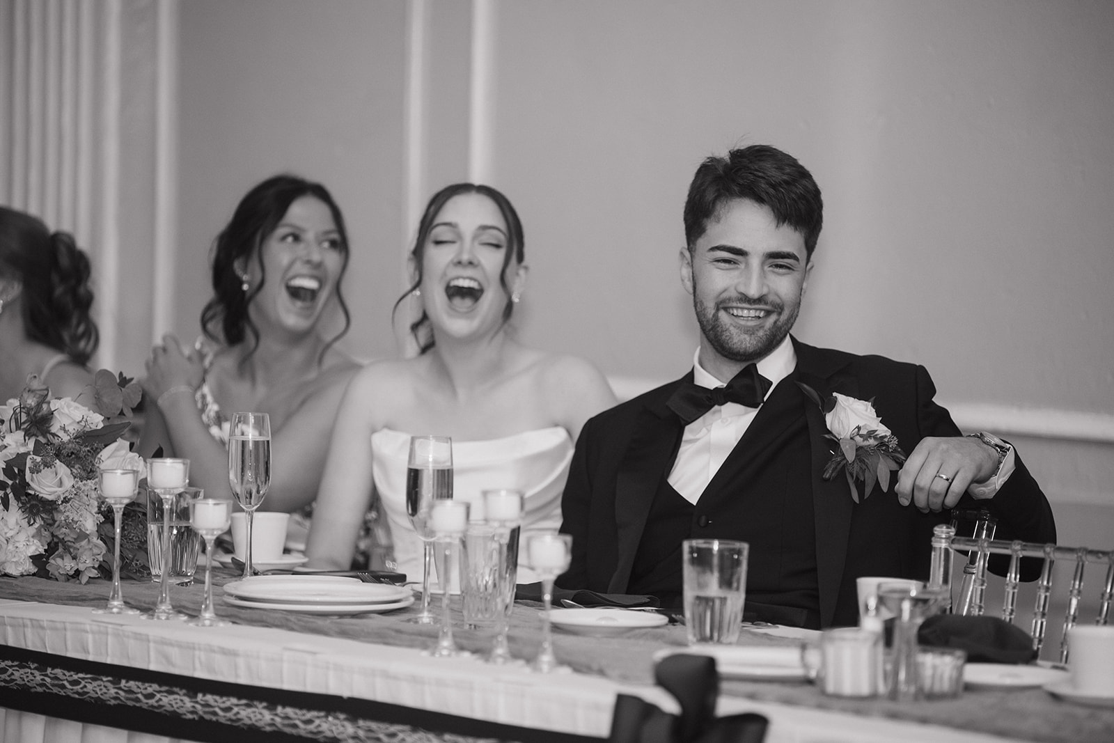 Black and white photo of a bride and groom laughing during speeches at Meeting House Grand Ballroom in Plymouth.