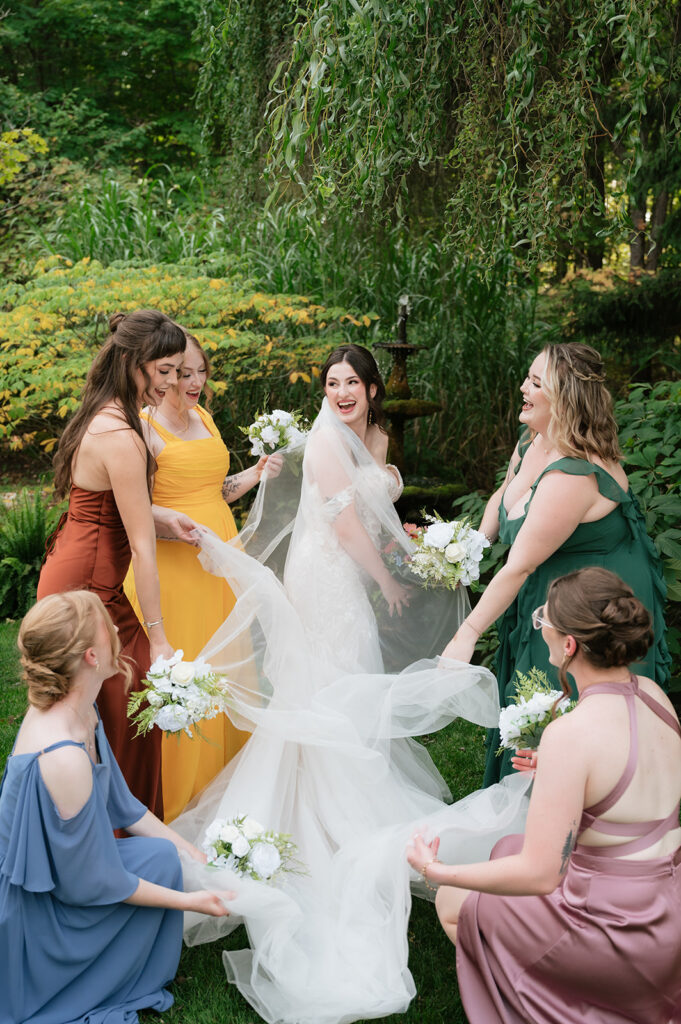 Bride laughing with bridesmaids wearing colorful jewel-toned dresses at an Owosso, Michigan wedding.