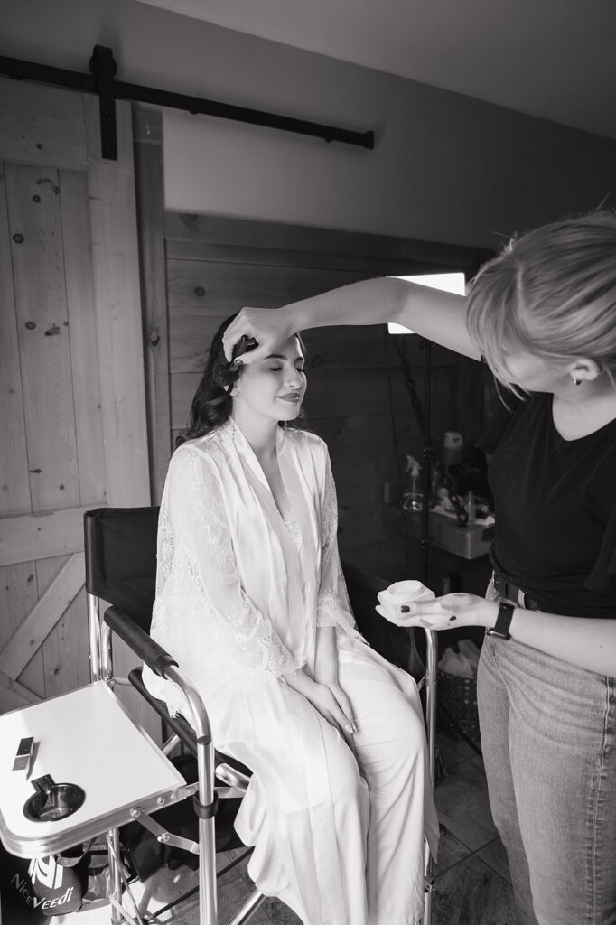 Black and white photo of a bride getting her makeup done for her wedding day.