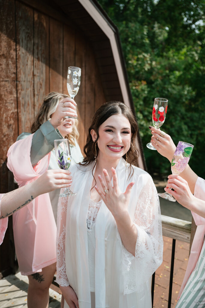 Bride smiling as the bridesmaids hold champagne glasses around her. 