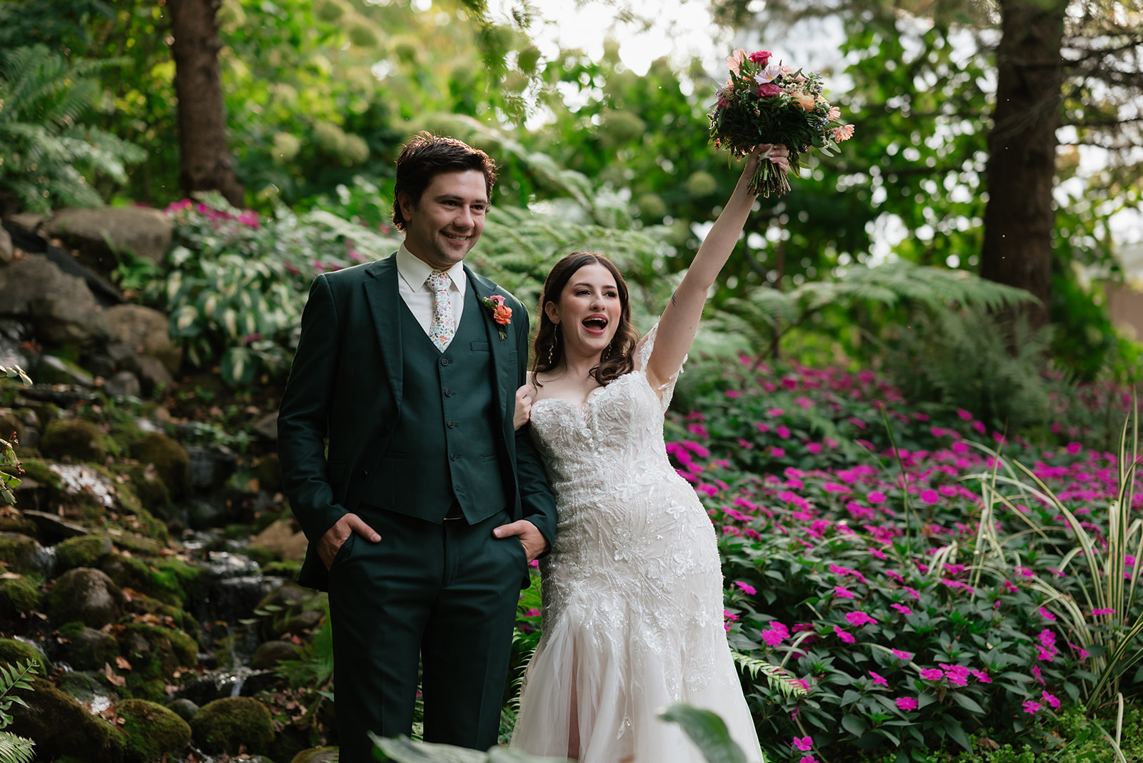 Bride and groom surrounded by ferns, colorful flowers, and a waterfall at Everlastings in the Wildwood.