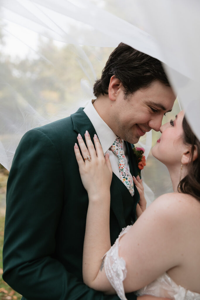 Bride and groom touching noses and smiling under the brides veil for portraits. 