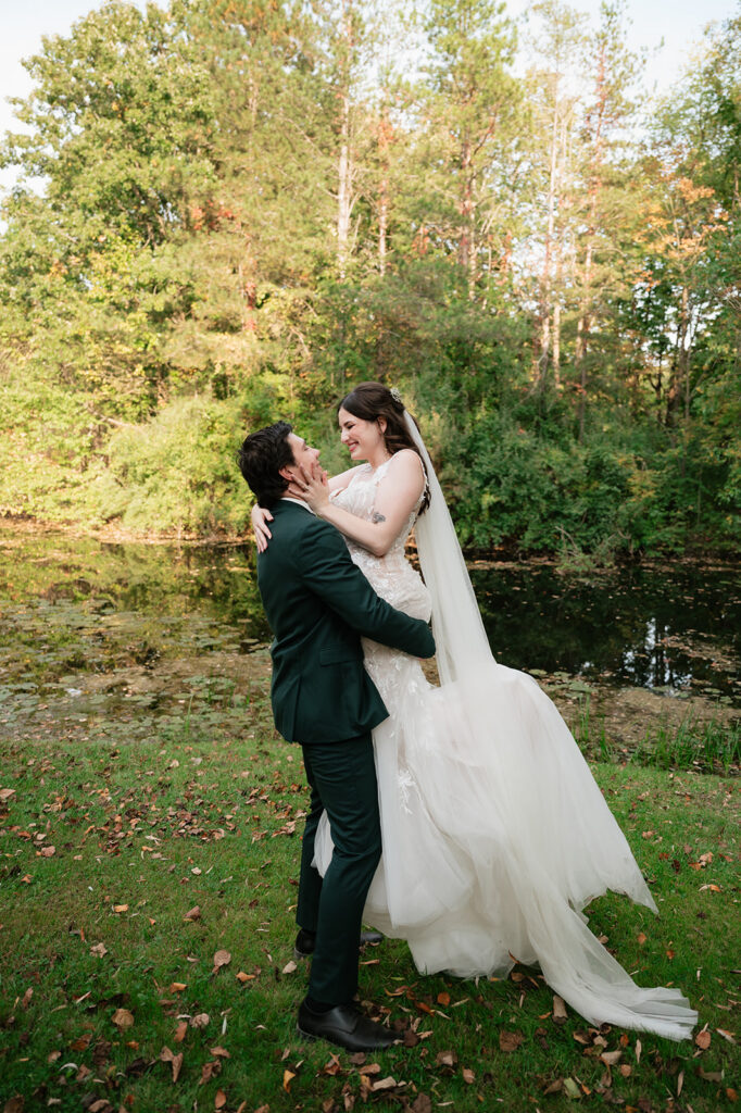 Groom lifting the bride next to a pond at Everlastings in the Wildwood.