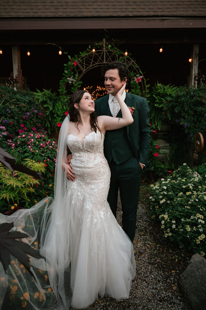 Bride and groom sharing a romantic moment among colorful flowers outside the greenhouse venue.