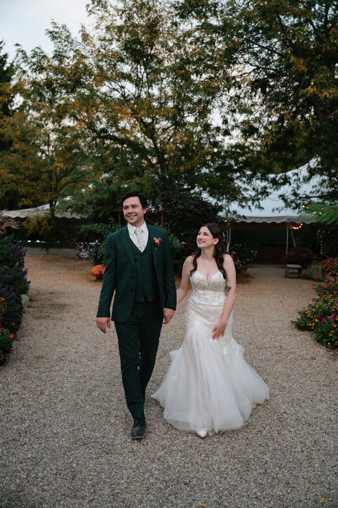 Bride and groom walking hand in hand through Everlastings in the Wildwood.