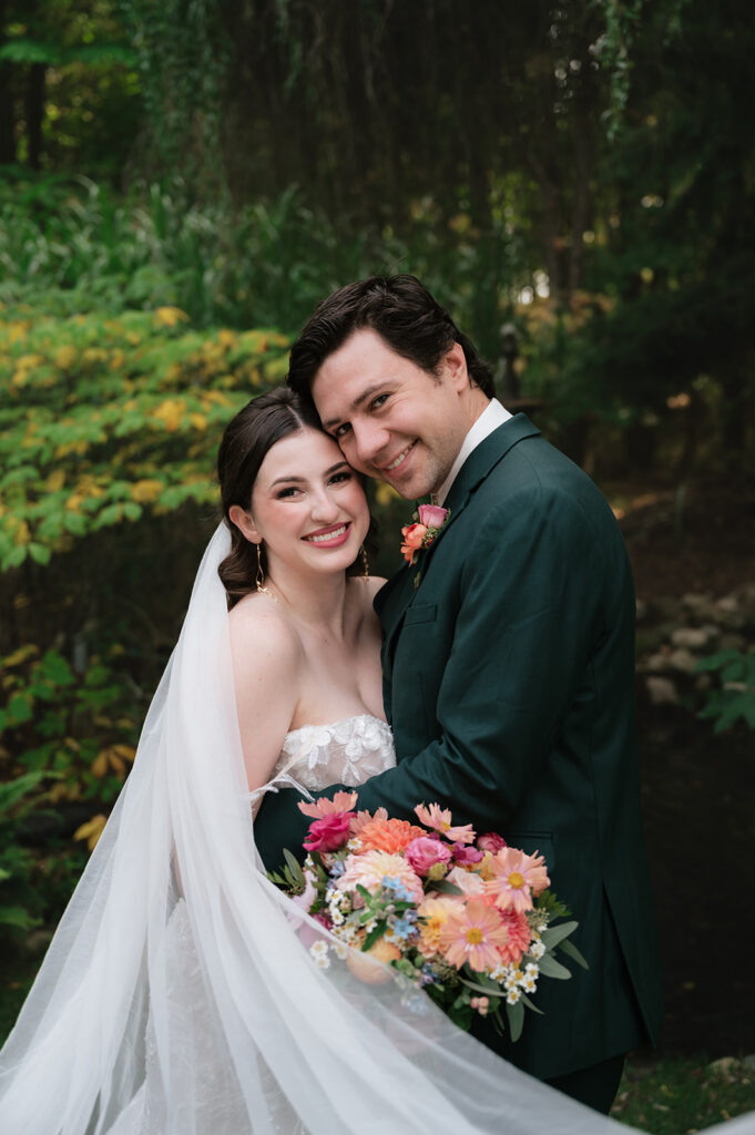 Bride and groom smiling at the camera during their Everlastings in the Wildwood wedding photos. 