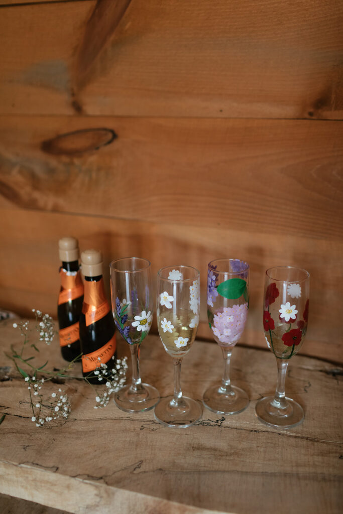 Hand-painted floral champagne glasses displayed with bottles and small flowers.