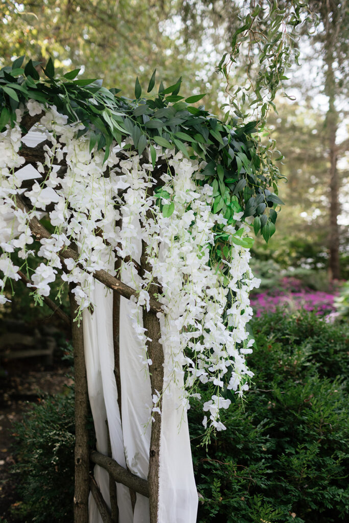 Rustic ceremony arbor decorated with white flowers and greenery in the garden.