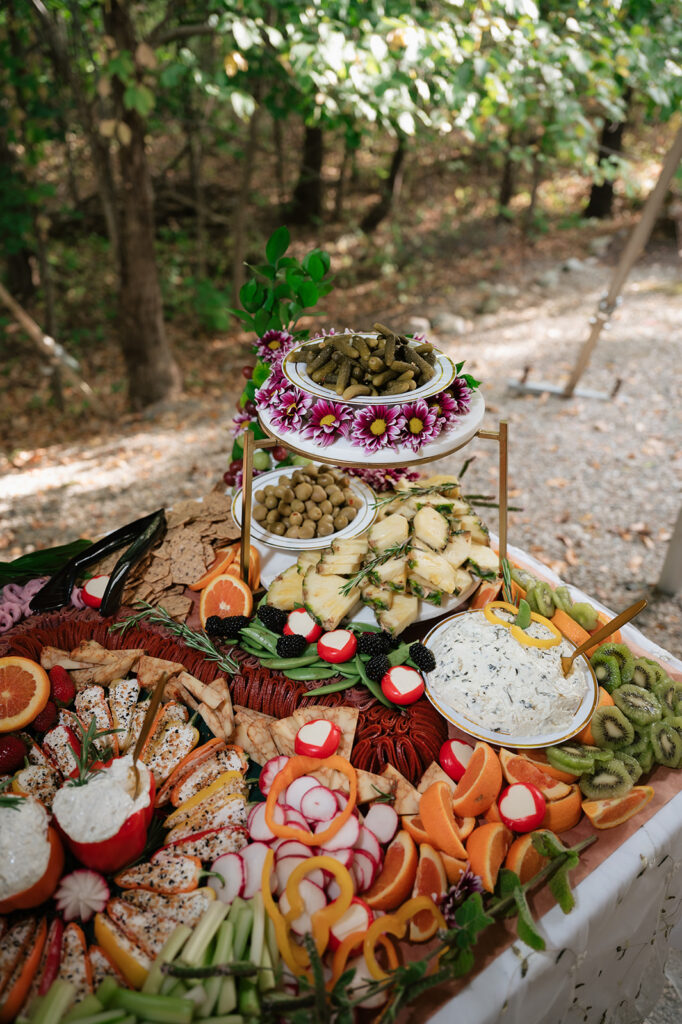 Close-up of a wedding grazing table with pickles, olives, pineapple, fruit, dips, and vegetables.