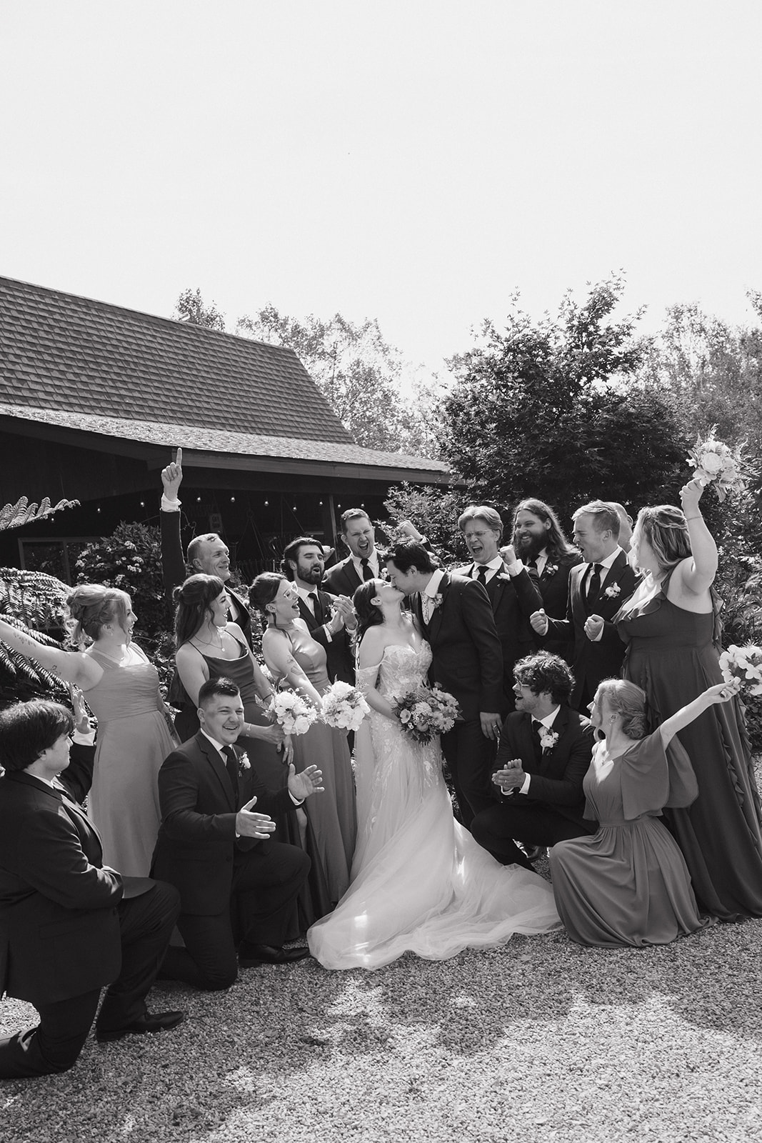 Black and white photo of the bride and groom kissing surrounded by their wedding party for their Everlastings in the Wildwood wedding photos.