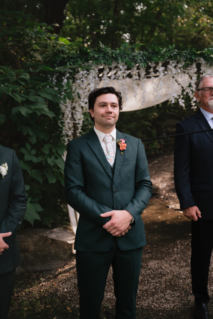 Groom reacting as the bride walks down the aisle during their garden wedding.