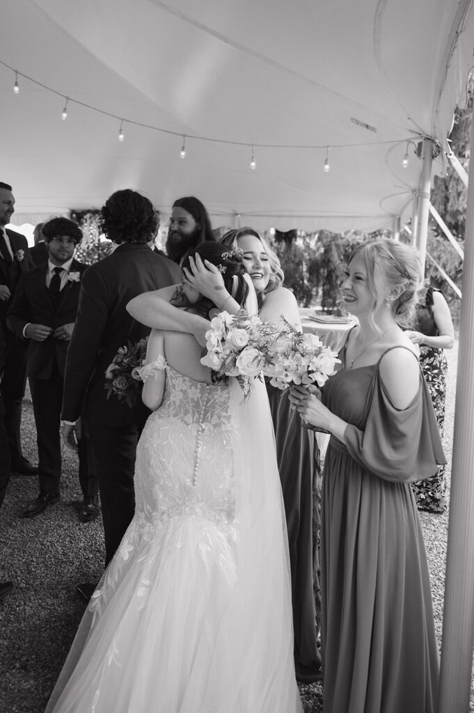 Black and white candid photo of a bride hugging her bridesmaids after the ceremony.