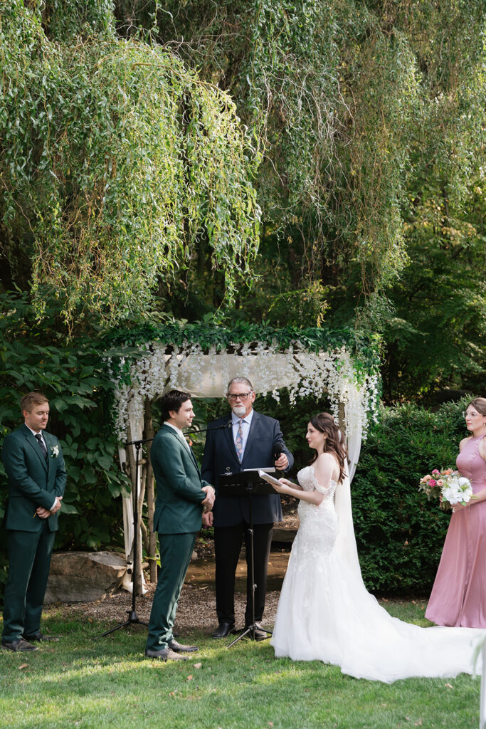 Bride and groom exchanging vows beneath a floral ceremony arbor.