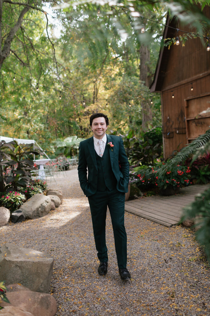 Groom wearing a dark green three-piece suit during outdoor wedding portraits in the garden.