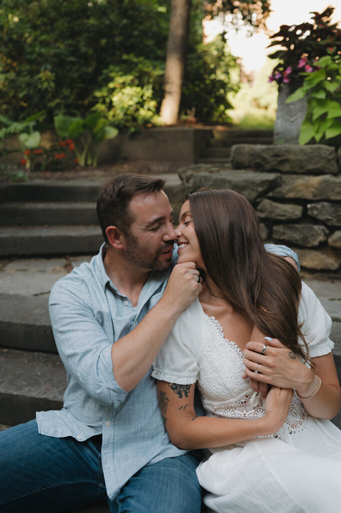 Couple going in for a kiss as they sit on the steps at Aquinas College for their Grand Rapids engagement photos.