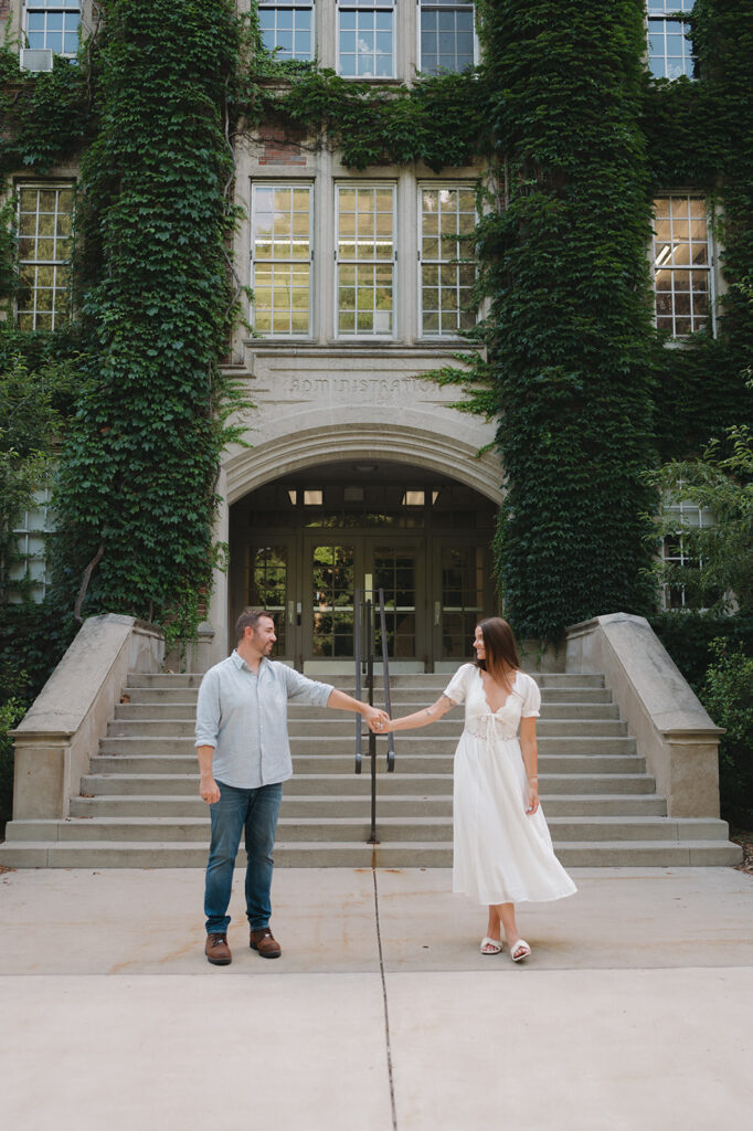 Couple holding hands in front of Aquinas College for their Grand Rapids engagement photos.