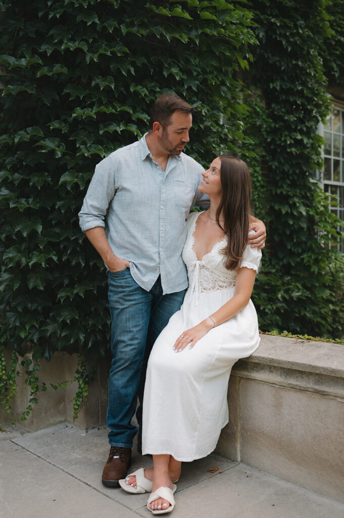 Woman sitting and looking up at her fiancé during their engagement session.