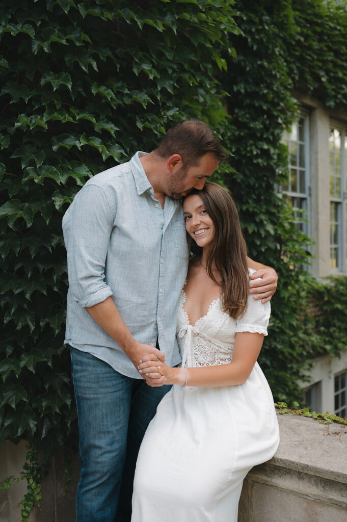 Man kissing his fiancés head as they pose for engagement photos.