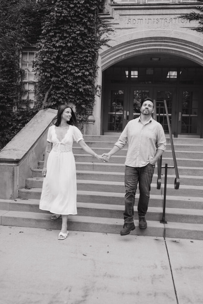 Black-and-white engagement photo of a couple walking down the campus steps.