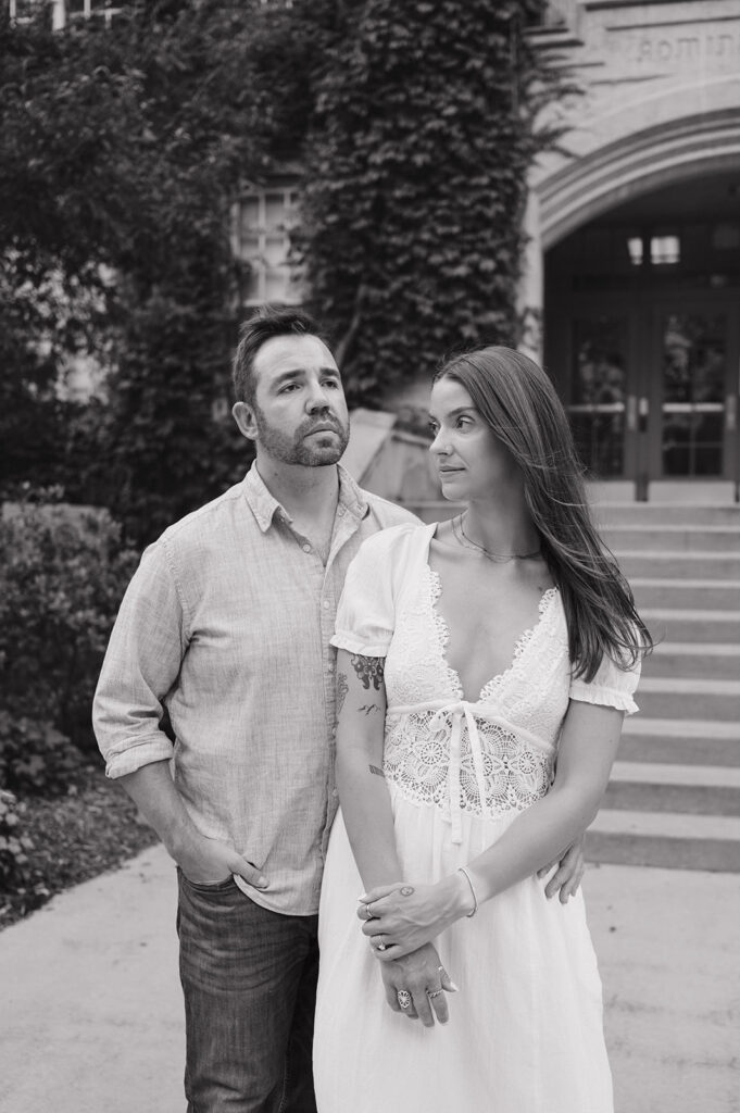 Black-and-white engagement photo of a couple posing together in front of the campus steps.
