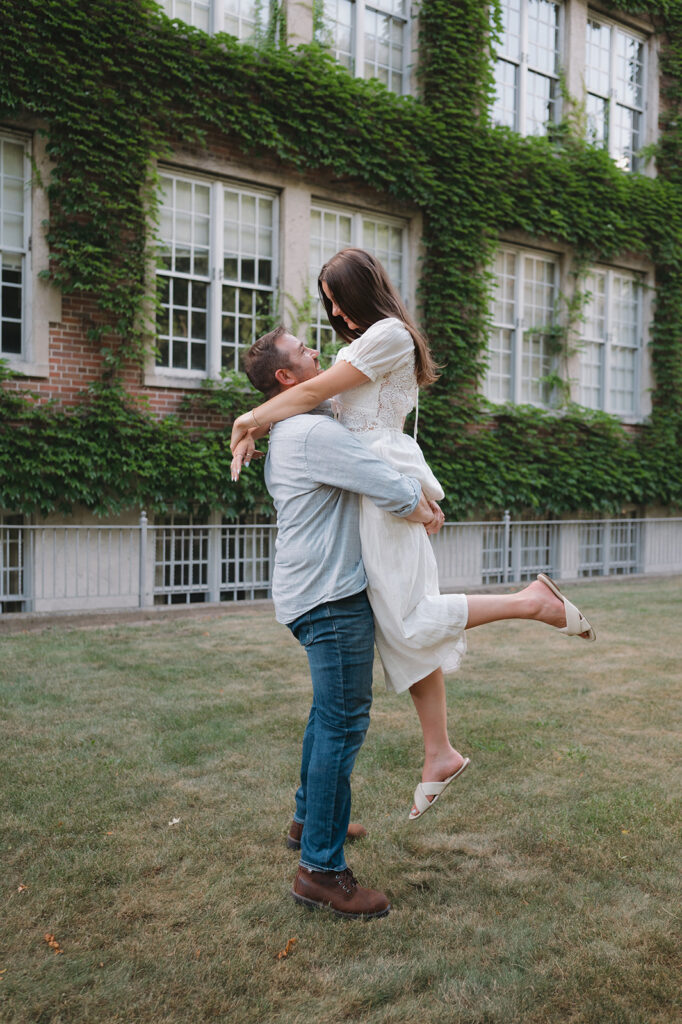 Man lifting his fiancé during their Gran Rapids engagement photos at Aquinas College.