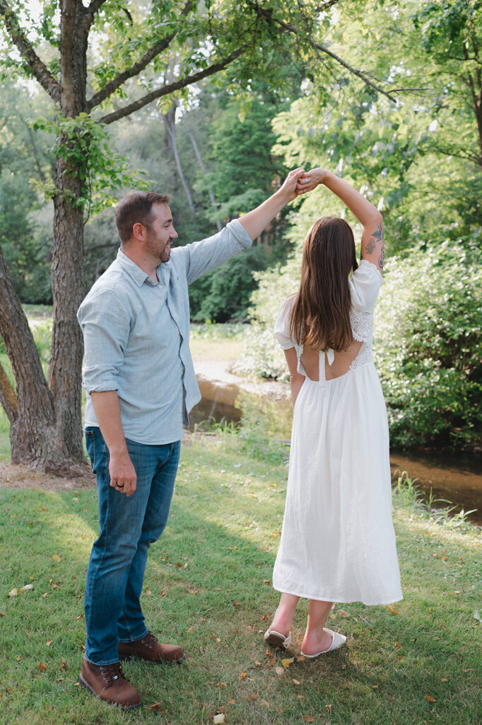 Man twirling his fiancé during their Grand Rapids engagement photos outdoors.