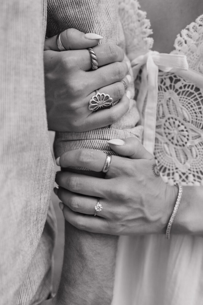 Close up black and white photo of a woman holding her fiancés arm and showing off her engagement ring.