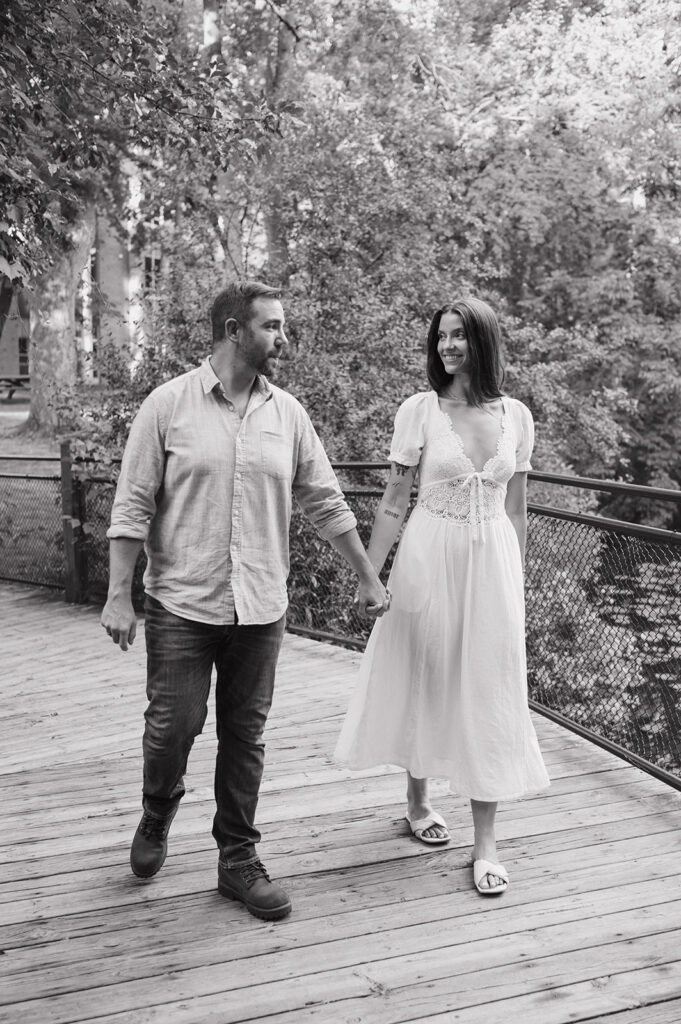 Black and white photo of a couple holding hands and walking over a bridge. 