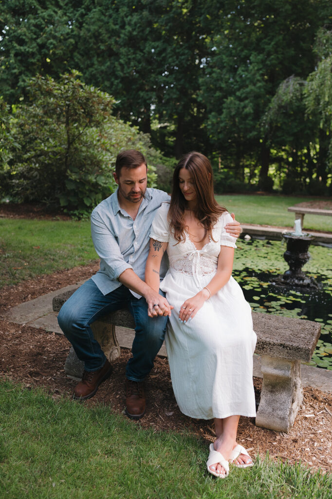 Couple sitting together beside a lily pond during their engagement session.