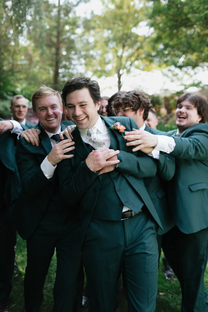 Groom laughing with his groomsmen during playful wedding party photos at Everlastings in the Wildwood.