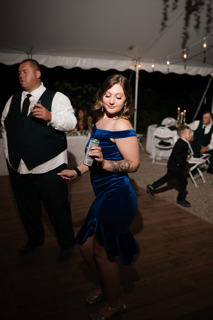 Guest in a blue dress dancing with a drink in hand.