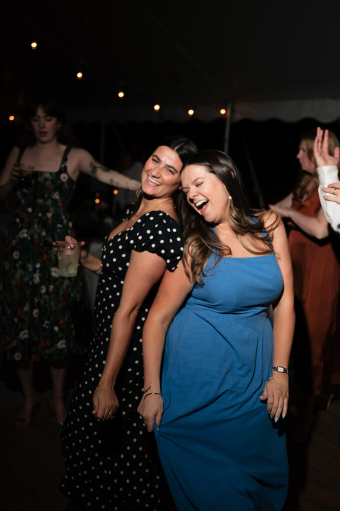 Two wedding guests laughing and dancing together during the evening reception.