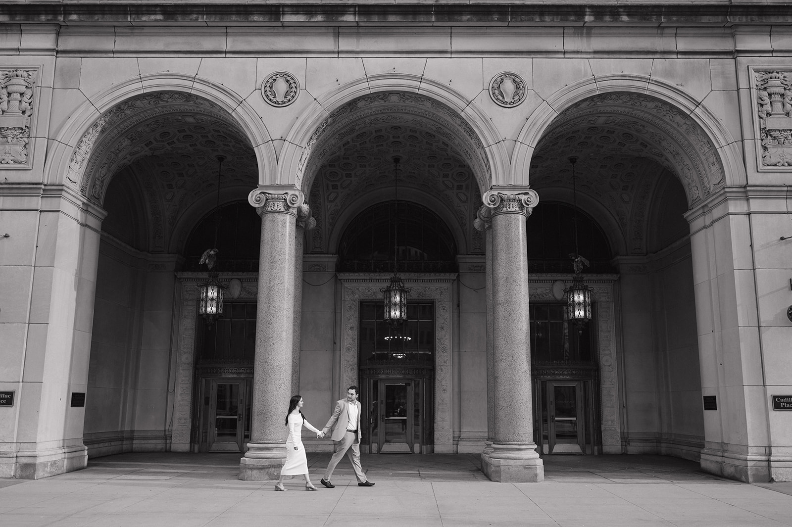 Black and white photo of a couple walking in front of Cadillac Place. 
