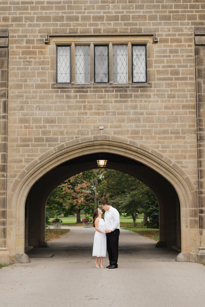 Couple posing under a building for their Ford House engagement photos in Grosse Pointe Shores, Michigan.